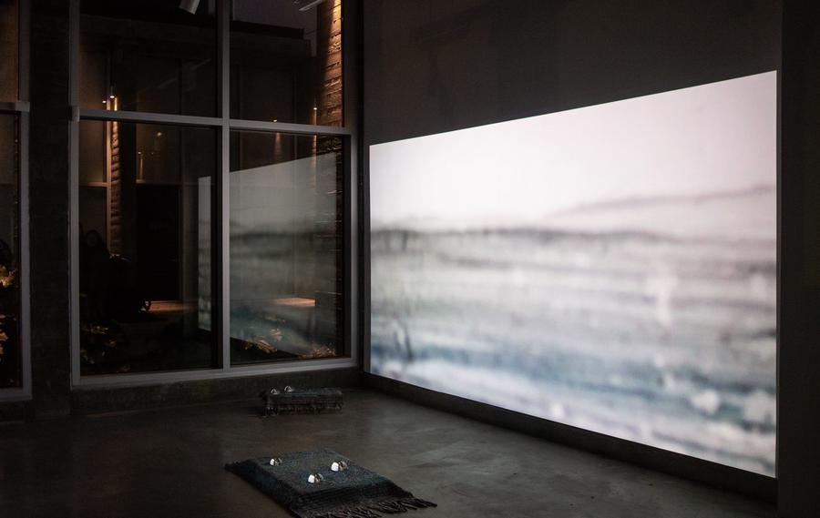 Installation view of large video projection that extends as a reflection in a window