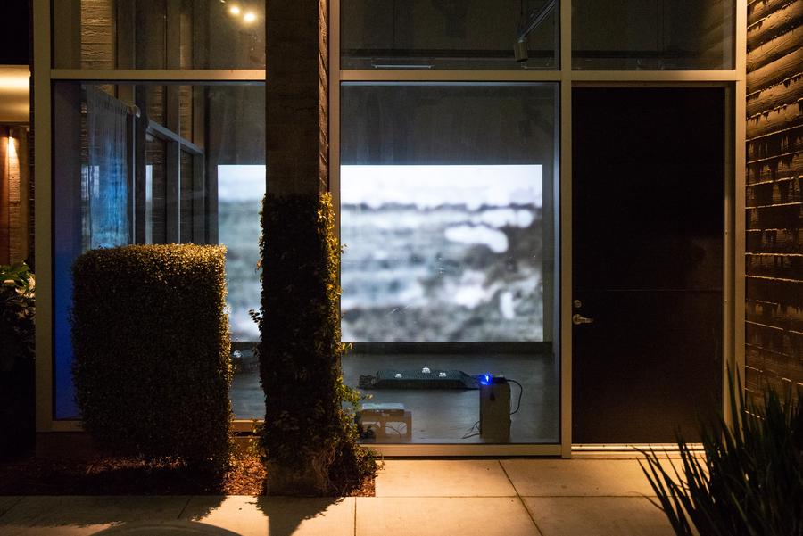 Installation view of large video projection as seen through front windows of gallery space